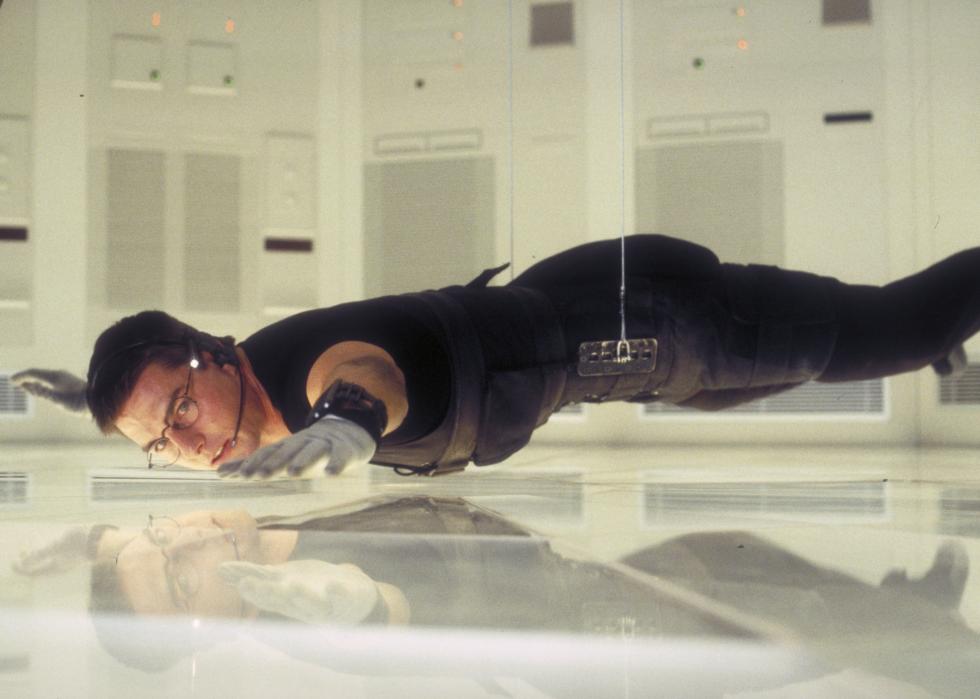 Tom Cruise, wearing all black, hangs from wires in an all white room.