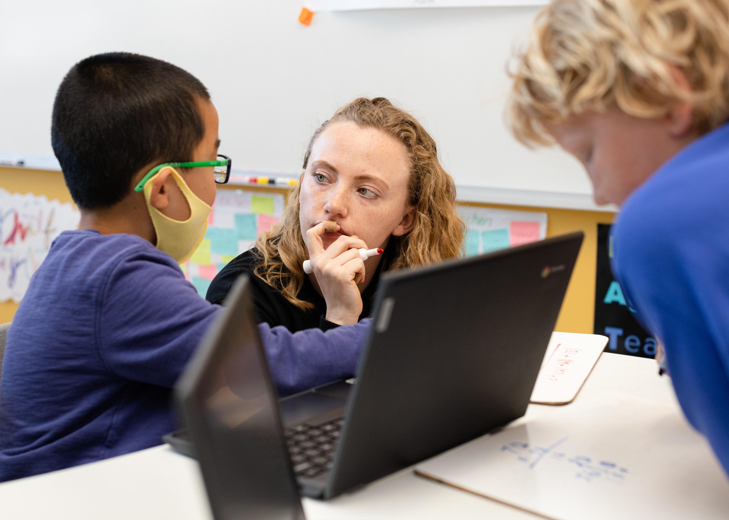 A young boy works with a teacher at his desk with a computer.