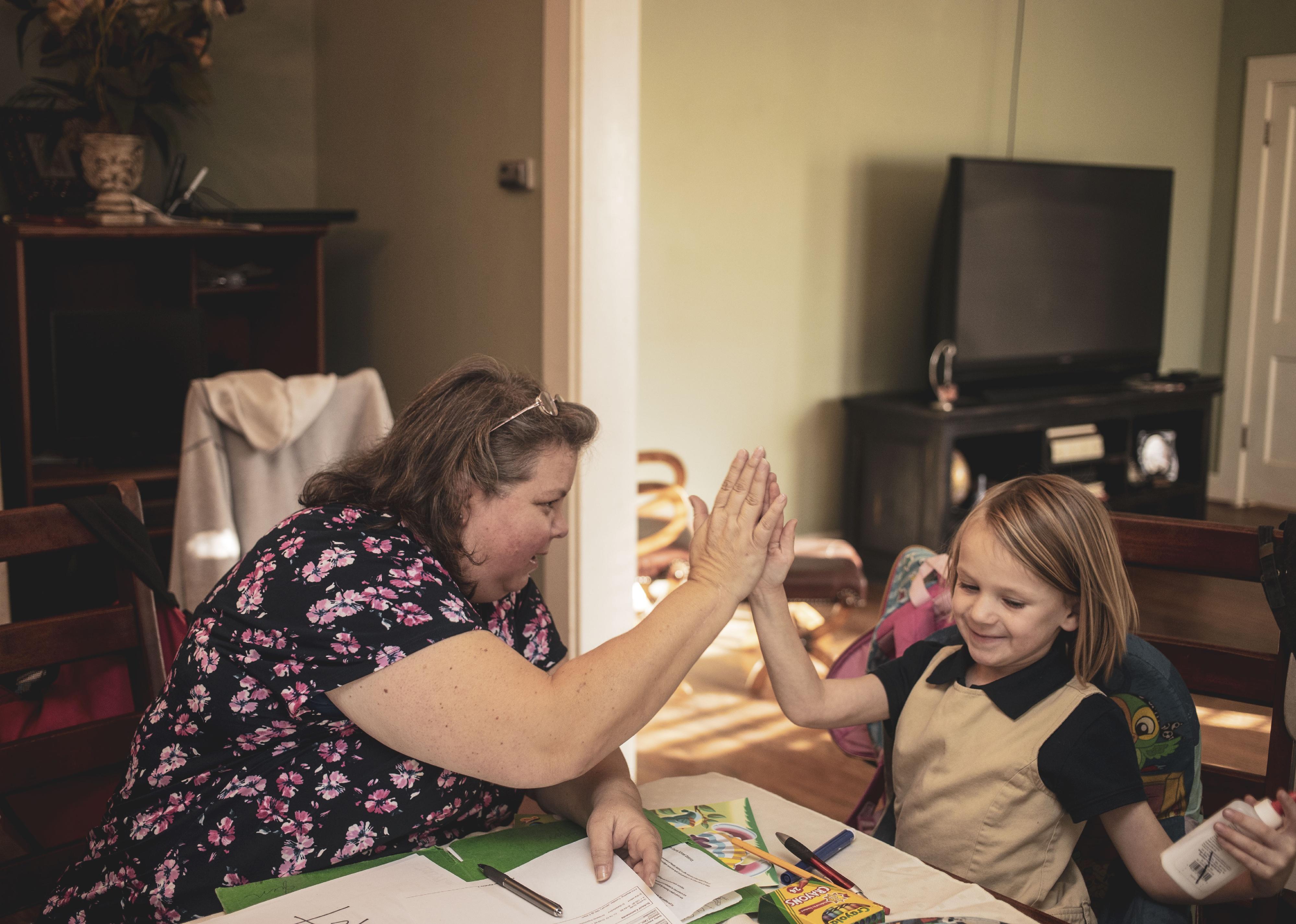 A mother gives her daughter a high-five at the kitchen table while doing homework.