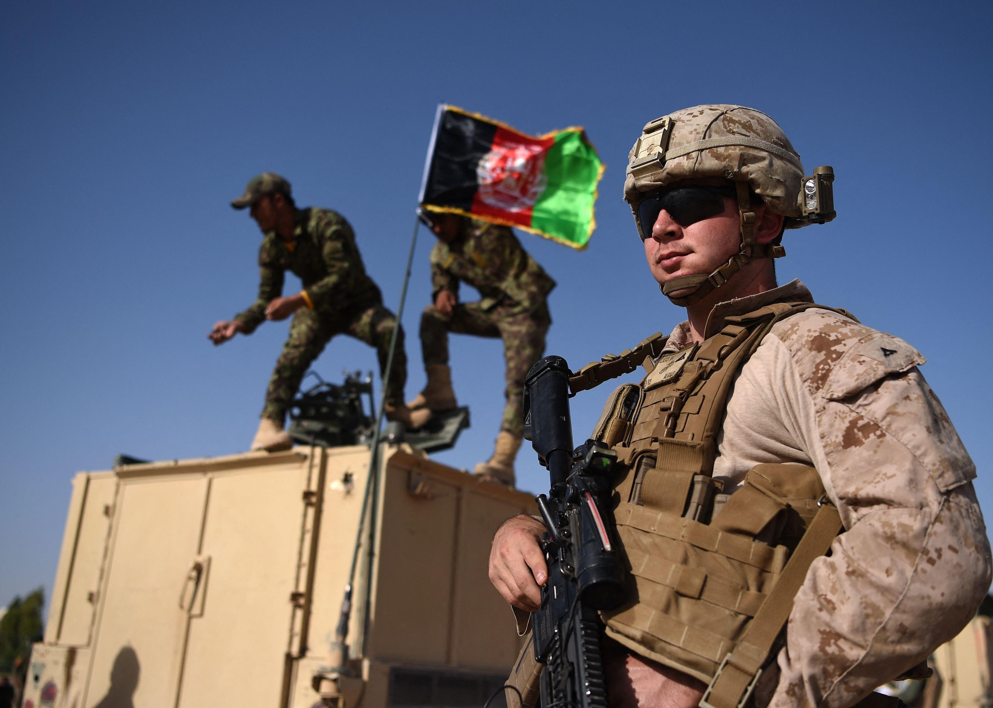 A US Marine looks on as Afghan National Army soldiers raise the Afghan National flag on an armed vehicle in the background.