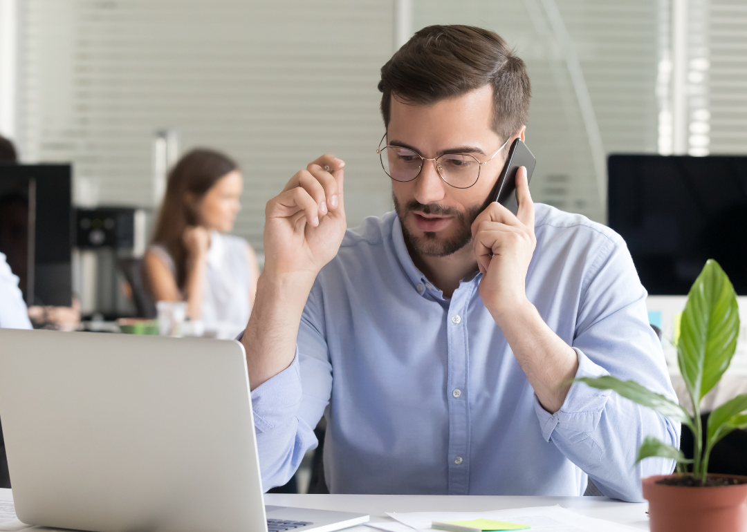 Man on phone looking at laptop.