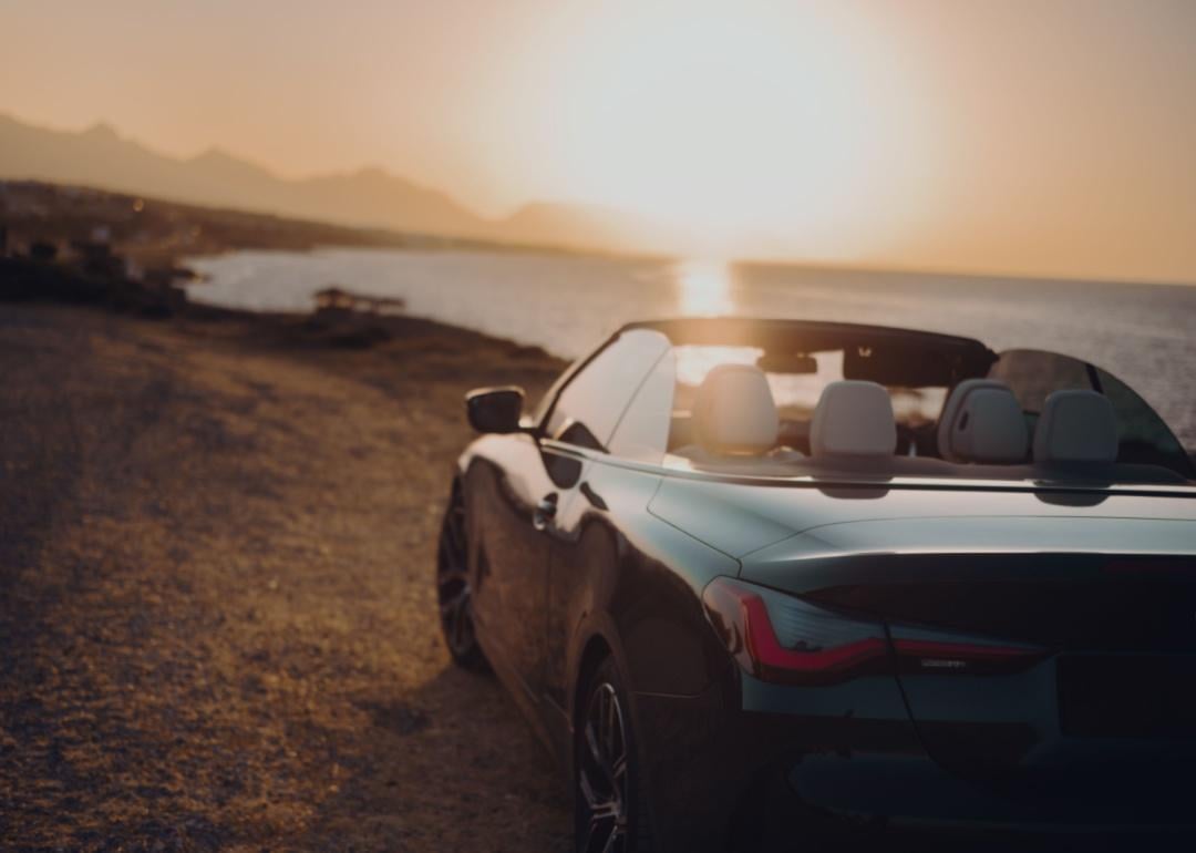 A black convertible by the sea at sunset.