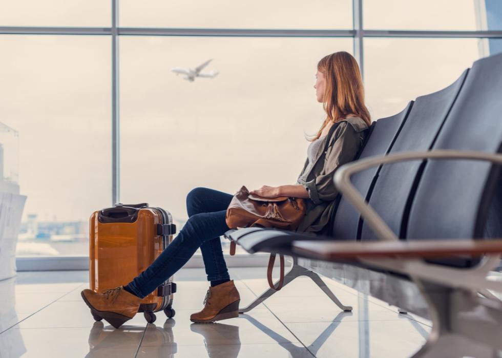 Woman sitting inside the airport watching an airplane takeoff.
