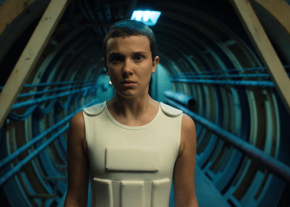 Millie Bobby Brown wearing a white vest in front of a tunnel.