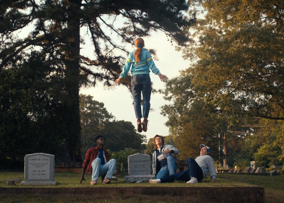 Sadie Sink levitating in front of Caleb McLaughlin, Joe Keery, and Gaten Matarazzo at a cemetery.