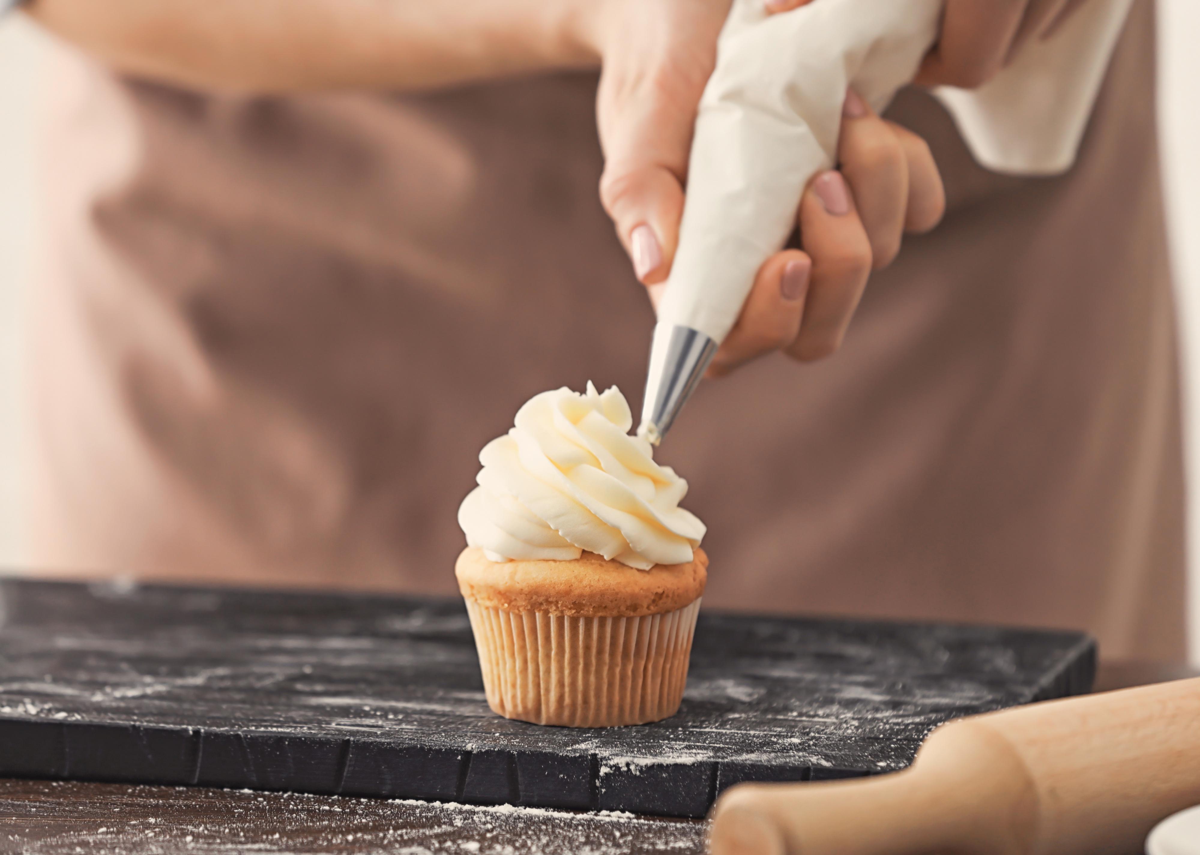 Woman decorating cupcake with frosting at table.