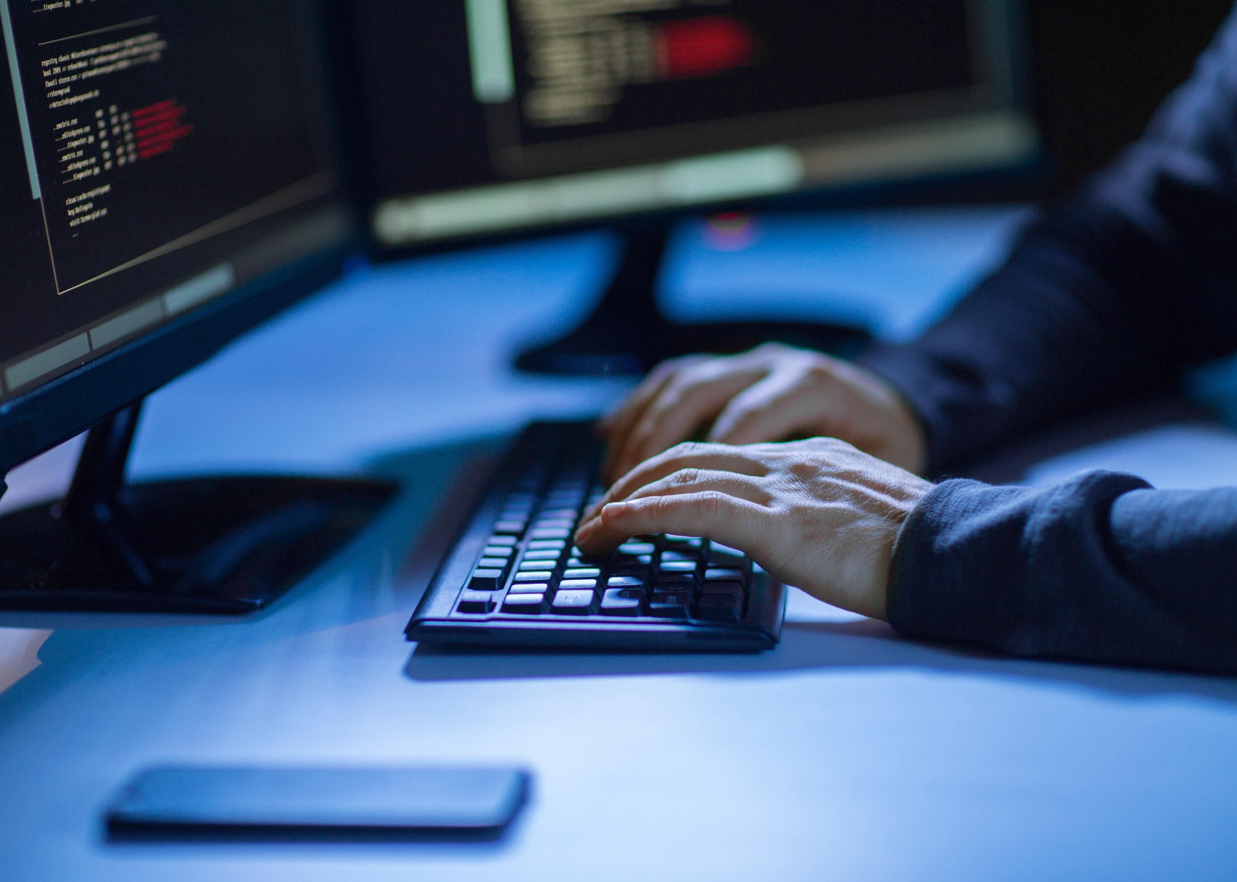 Hands of hacker in dark room using computer
