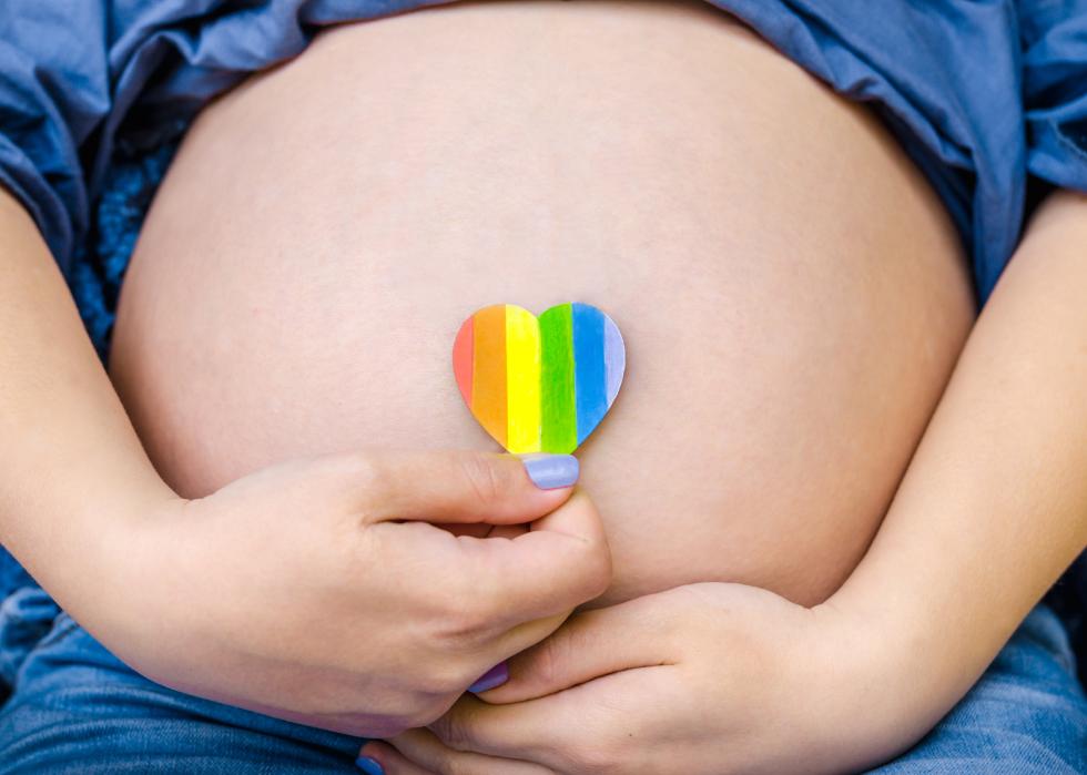Close up of woman's pregnant stomach with cutout of rainbow heart