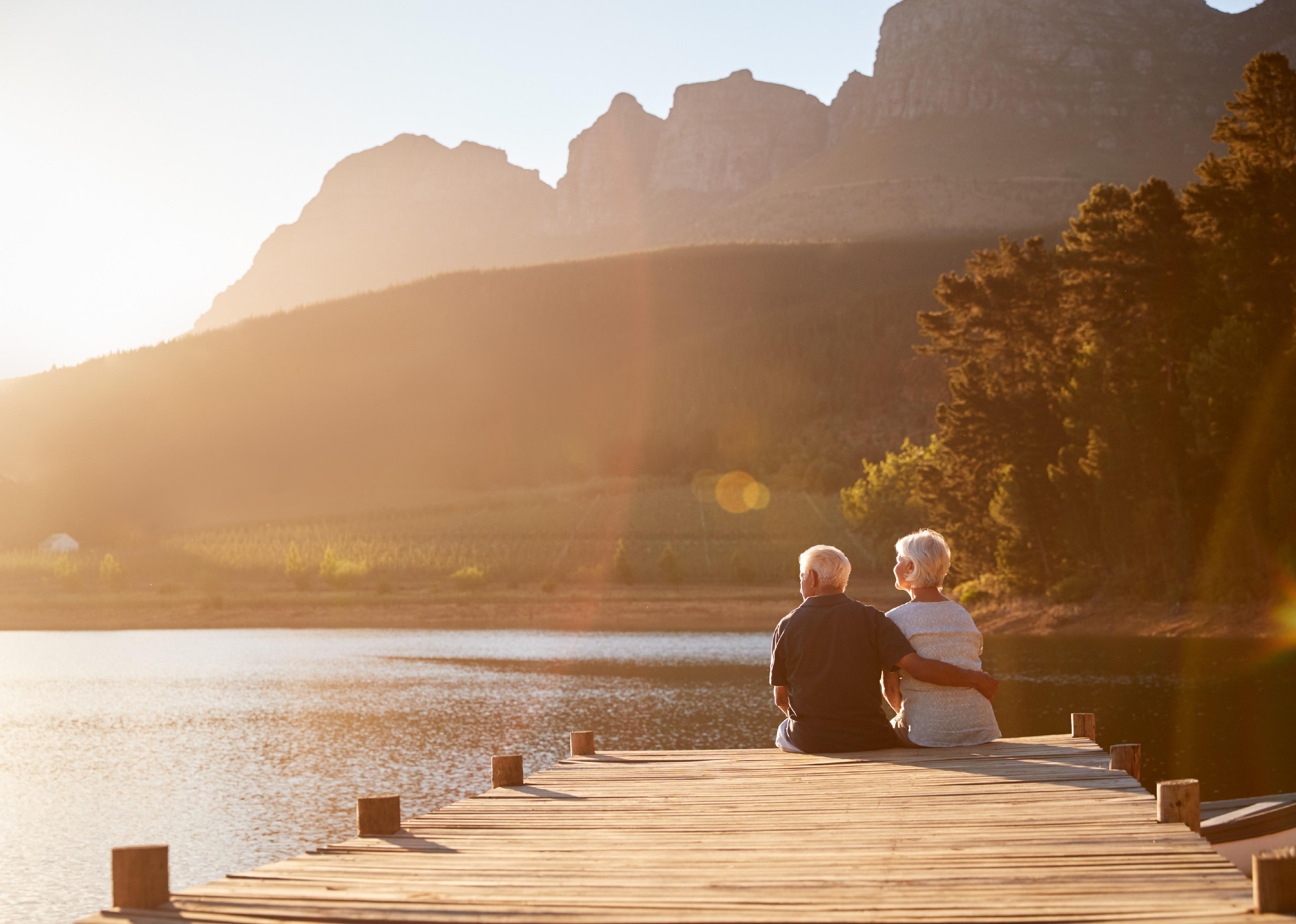 Senior couple sitting on a wooden dock by a lake.