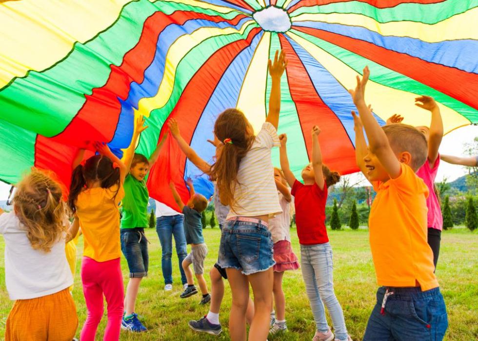 A group of children under a multicolored parachute tent.