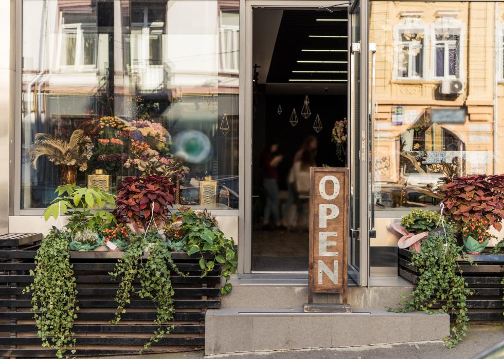 Open signboard, potted plants and reflecting windows at flower shop