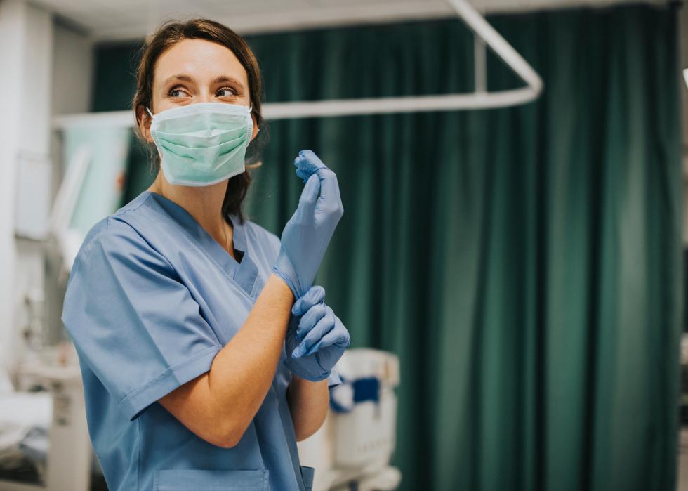 A nurse with a mask putting on gloves in a hospital.