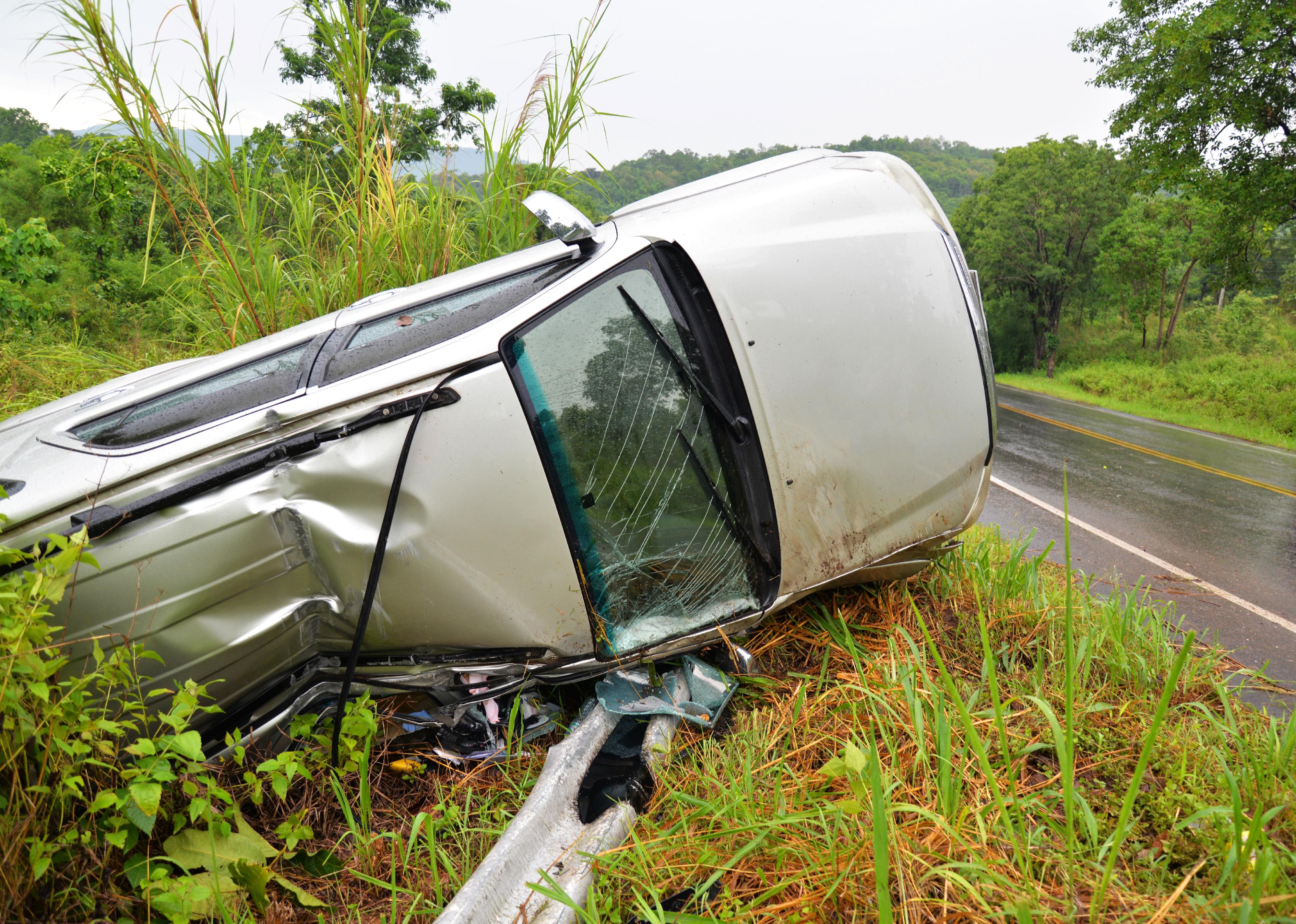 Car on its side next to a wet road.