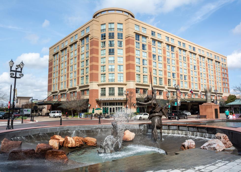 Sugar Land Town Square, with fountain, sculptures, building, city traffic and people.