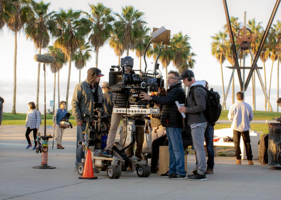 Wide view of Hollywood camera crew filming a scene with palm trees in the background