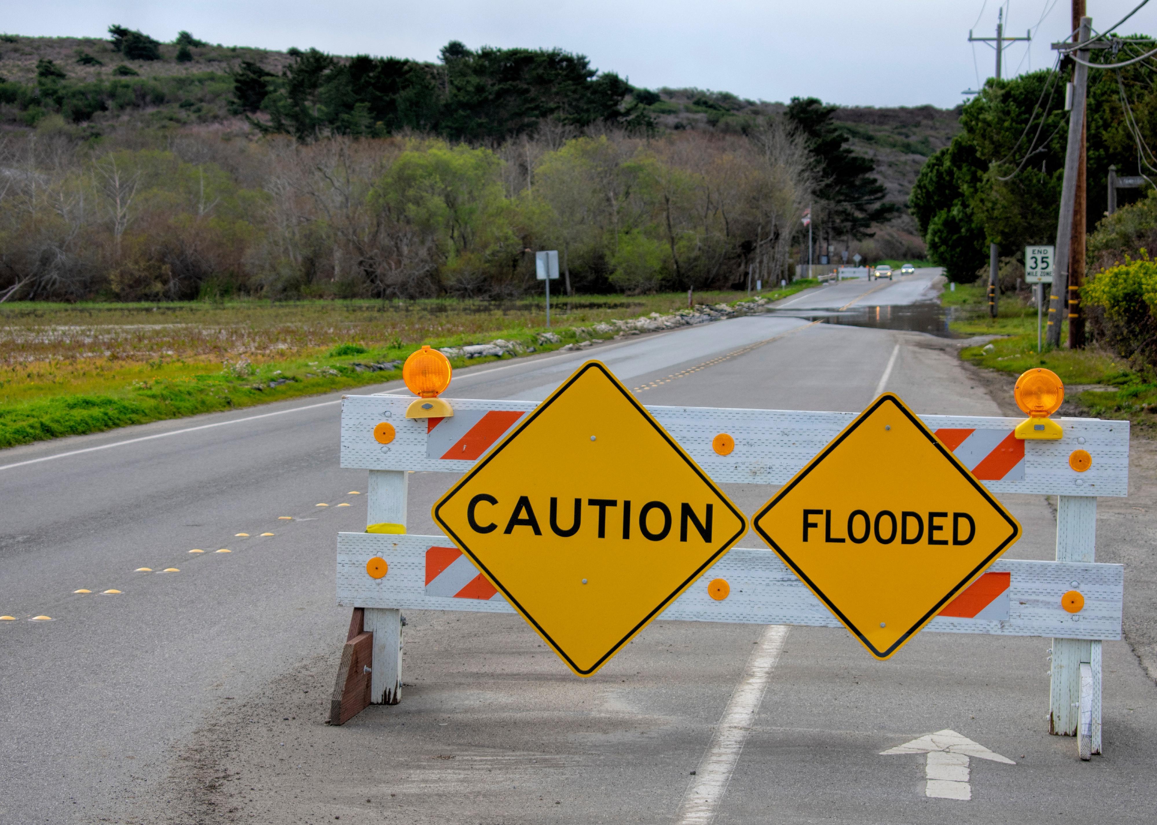 Yellow Caution and Flooded warning signs on barricade installed across two-way street.