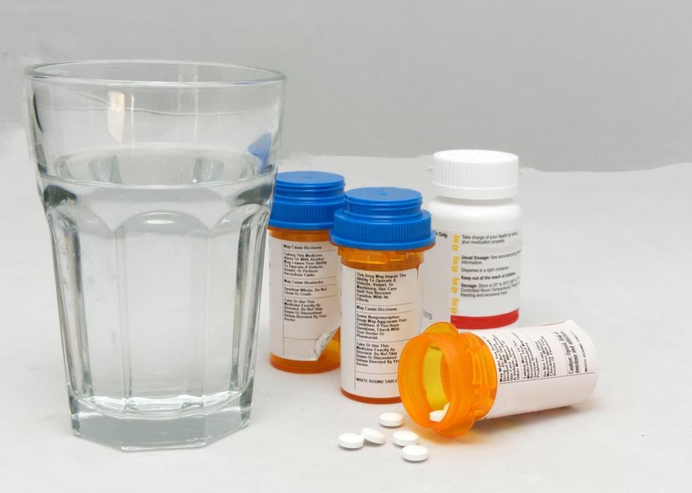 Opioid pill bottle with pills spilling out and placed with other pill bottles and glass of water.