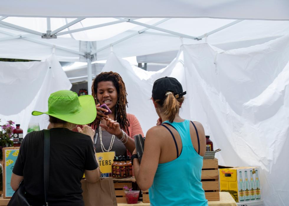 A vendor in a tented market takes a mobile payment from a customer.