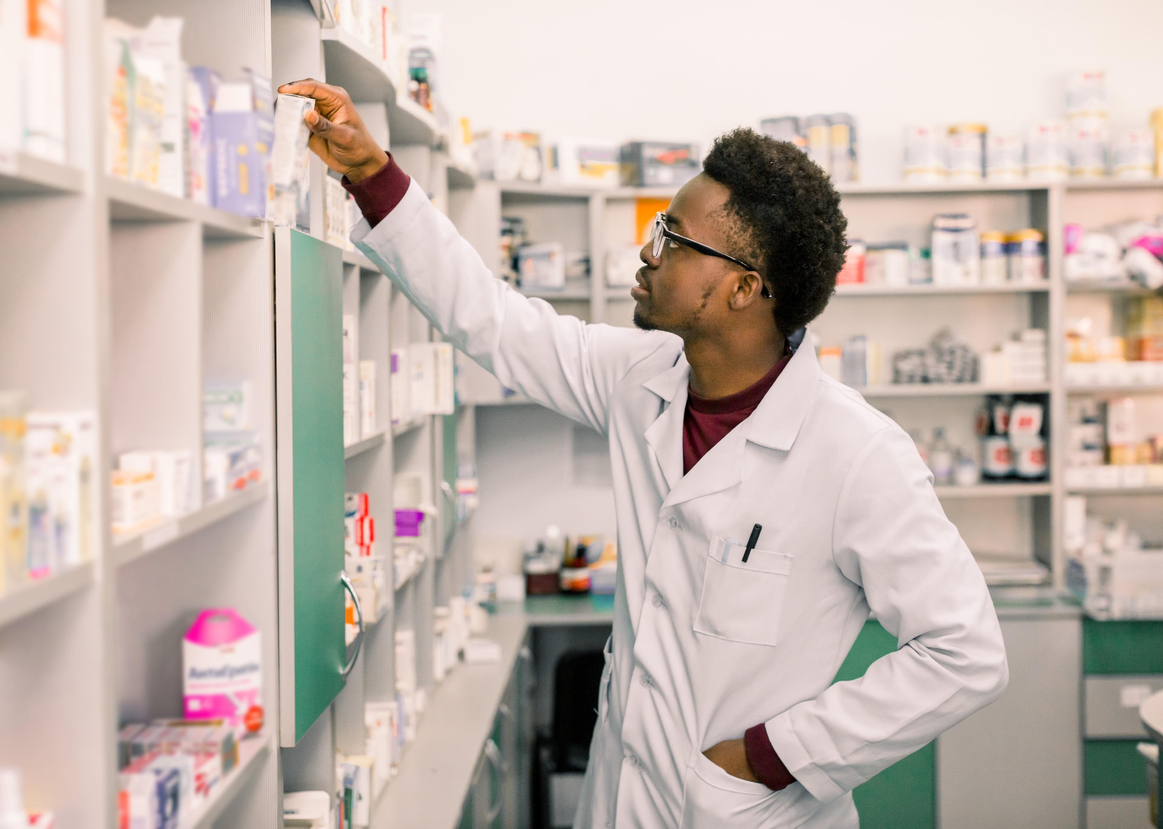 Pharmacist standing in interior of pharmacy and searching shelves.