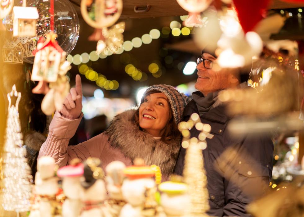 A smiling woman, standing next to a man, points at items at a holiday fair.