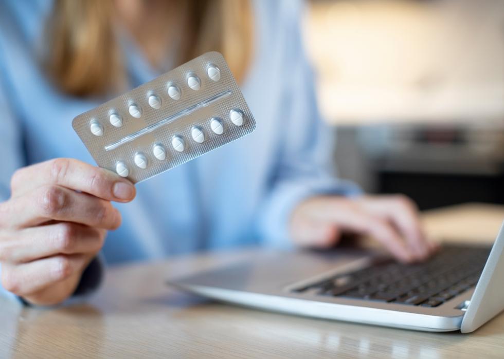 Close up of a person looking up a medication online, holding a blister pack of pills.