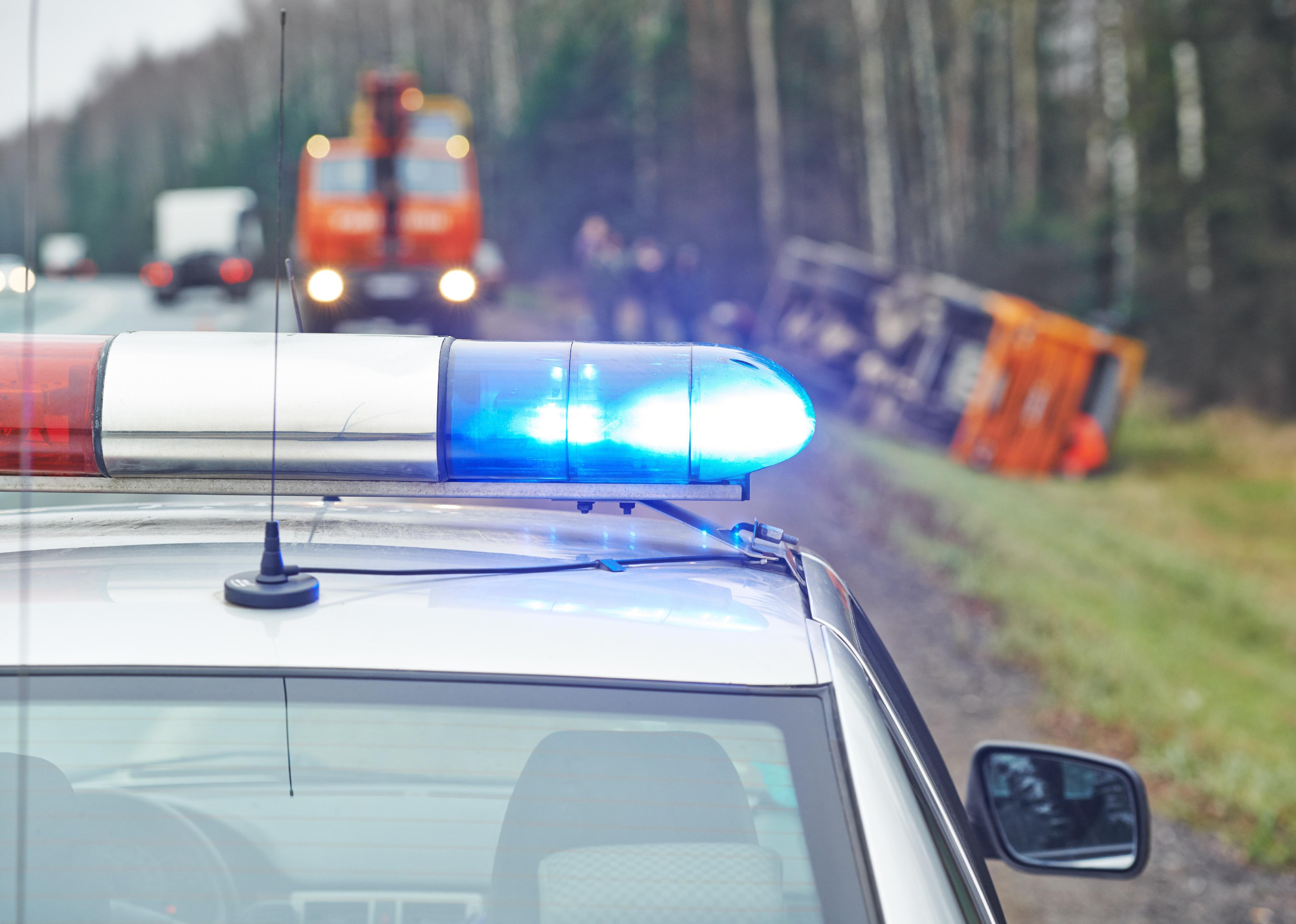 Police car with a flasher in front of damaged truck.