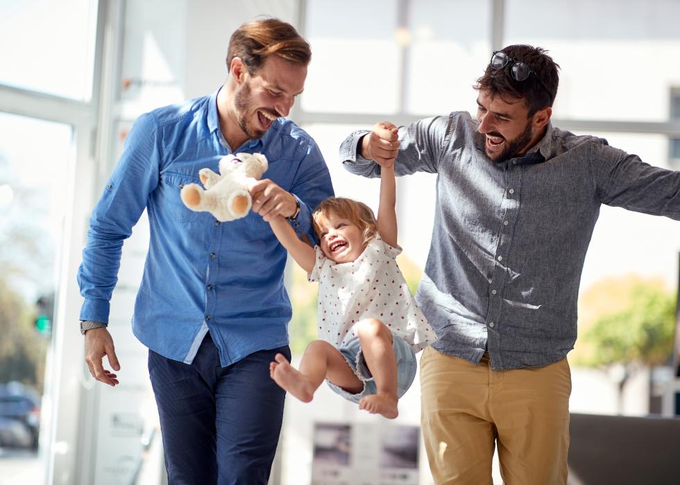 Two men laughing and swinging little girl between them