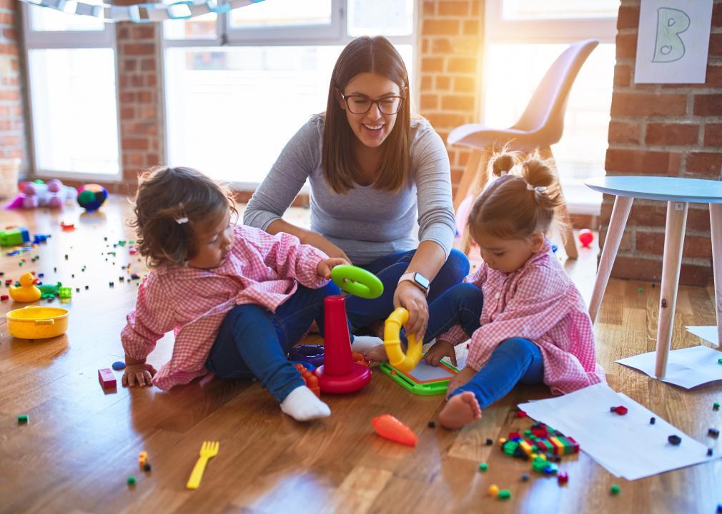 A childcare worker plays with two kids in a room filled with toys.