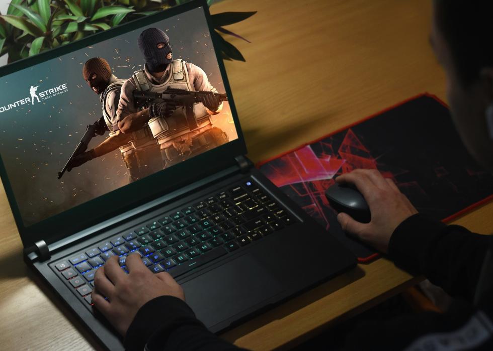 Hands on a laptop showing Counter-Strike: Global Offensive.