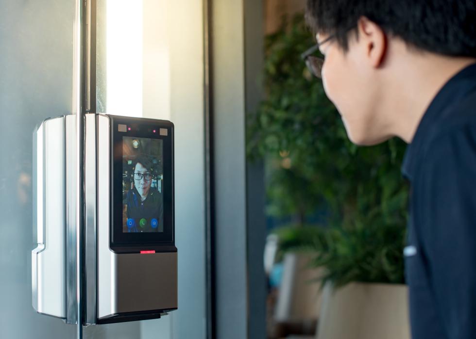 Man using face scanner to unlock glass door in office building.