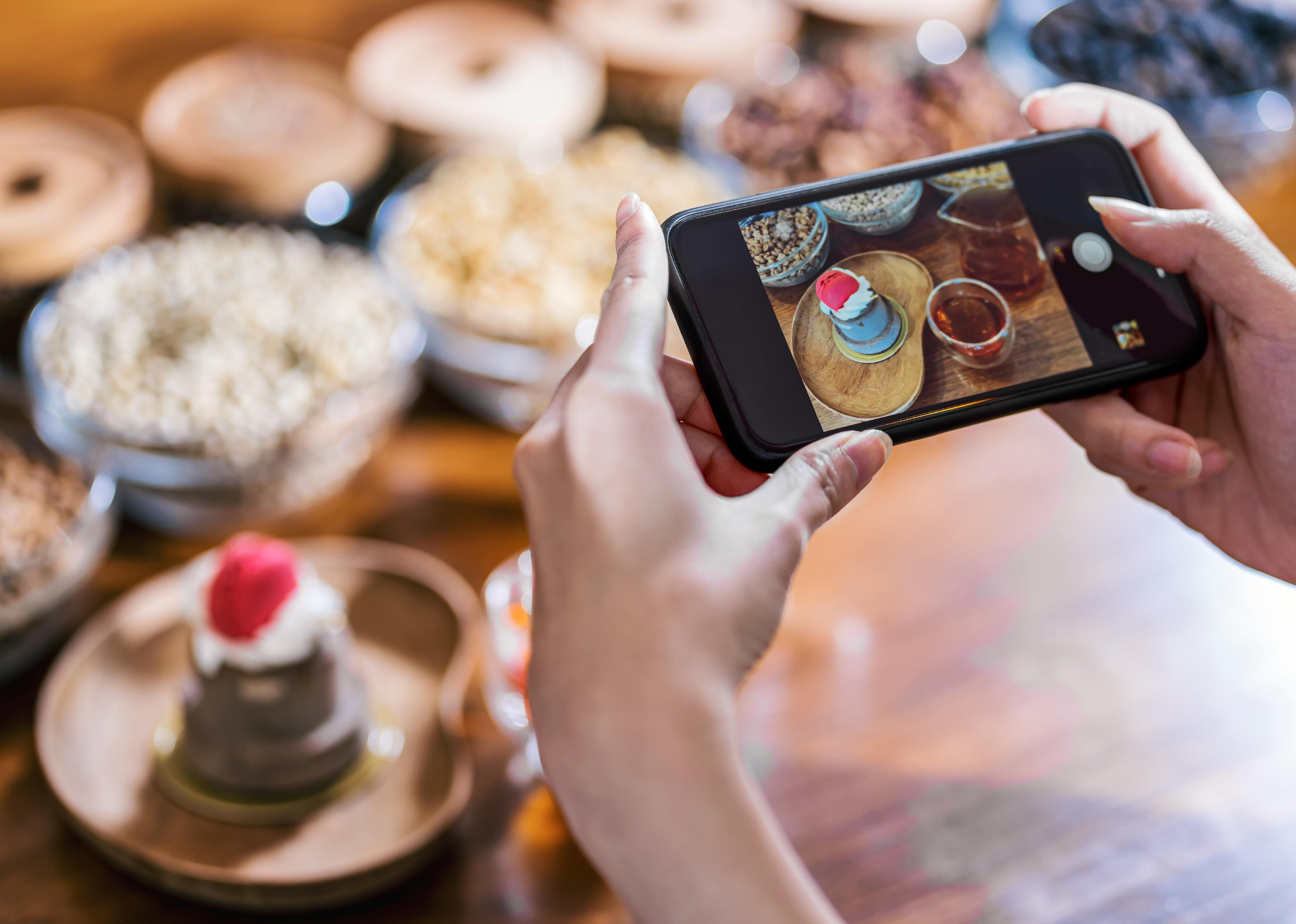 Close-up of a person with mobile phone taking photo of cupcake.