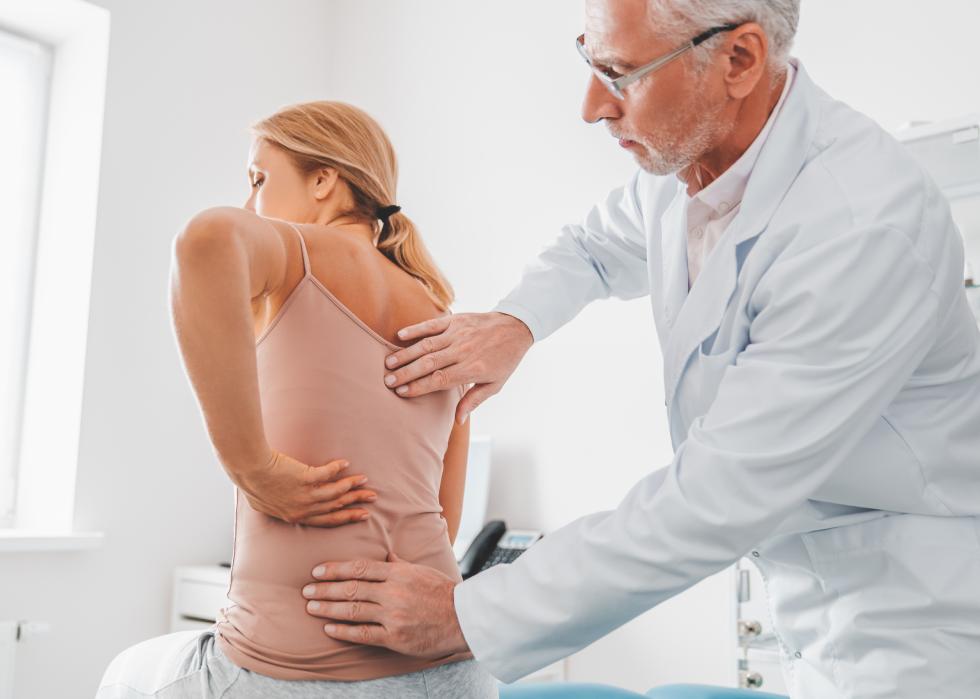 Senior male chiropractor examining patient's back in clinic.