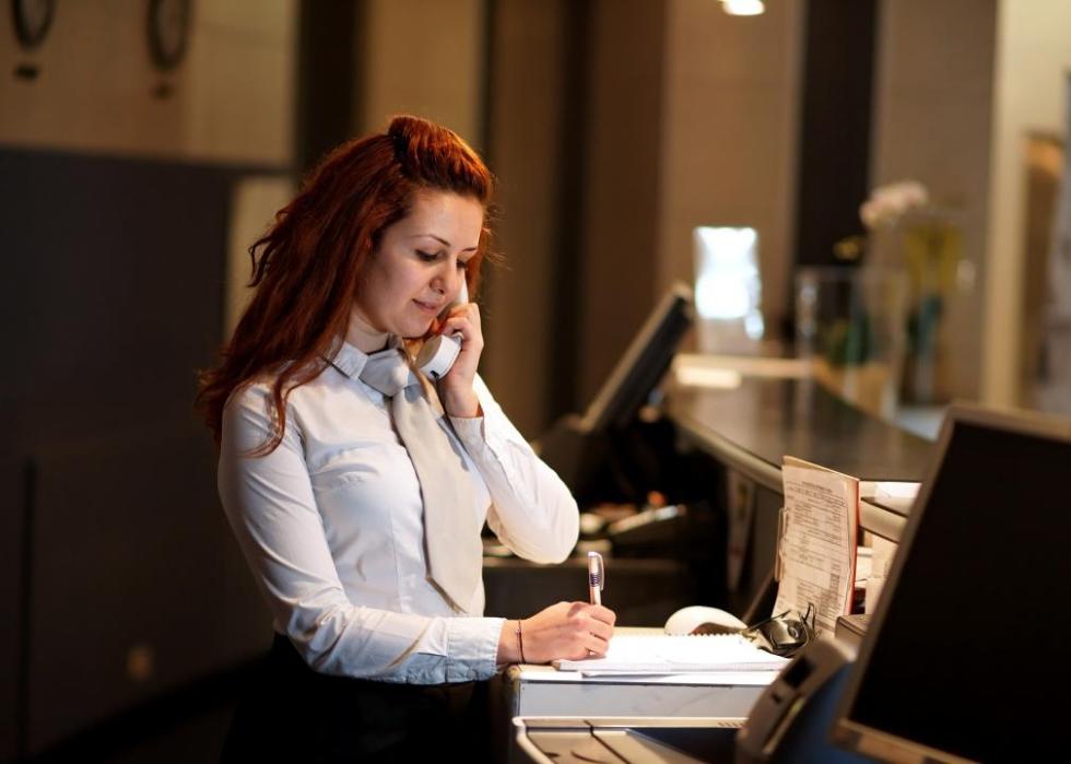 A woman answering the phone behind the front desk of an upscale hotel.