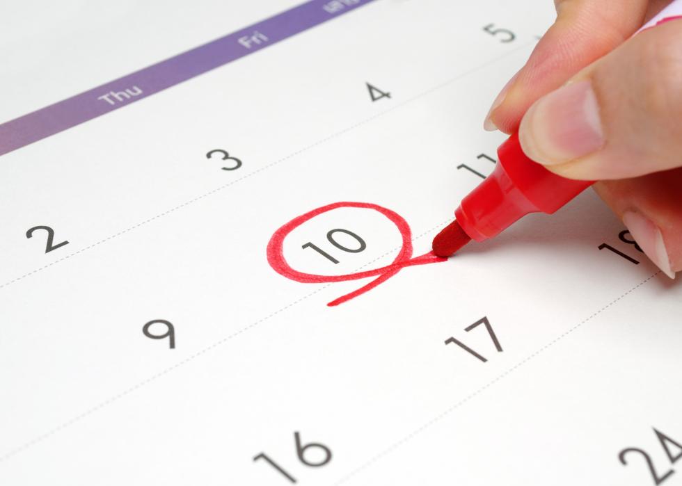 A close up of someone using a red marker to circle the 10th day on a paper calendar.