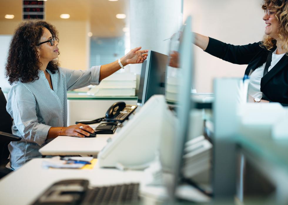 Woman standing at desk giving her card to the receptionist. 