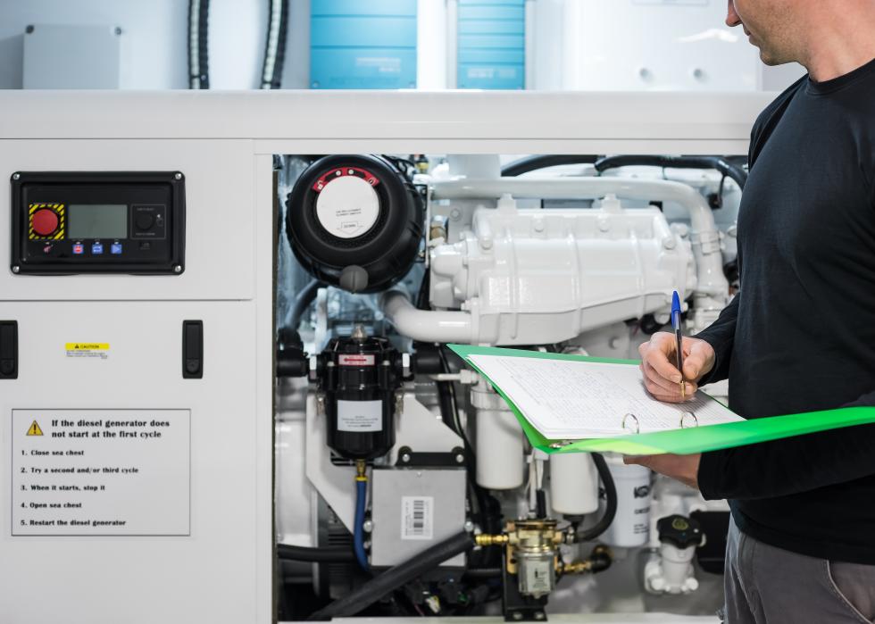 A man with a clipboard checking mechanics, writing on a piece of paper in a folder.