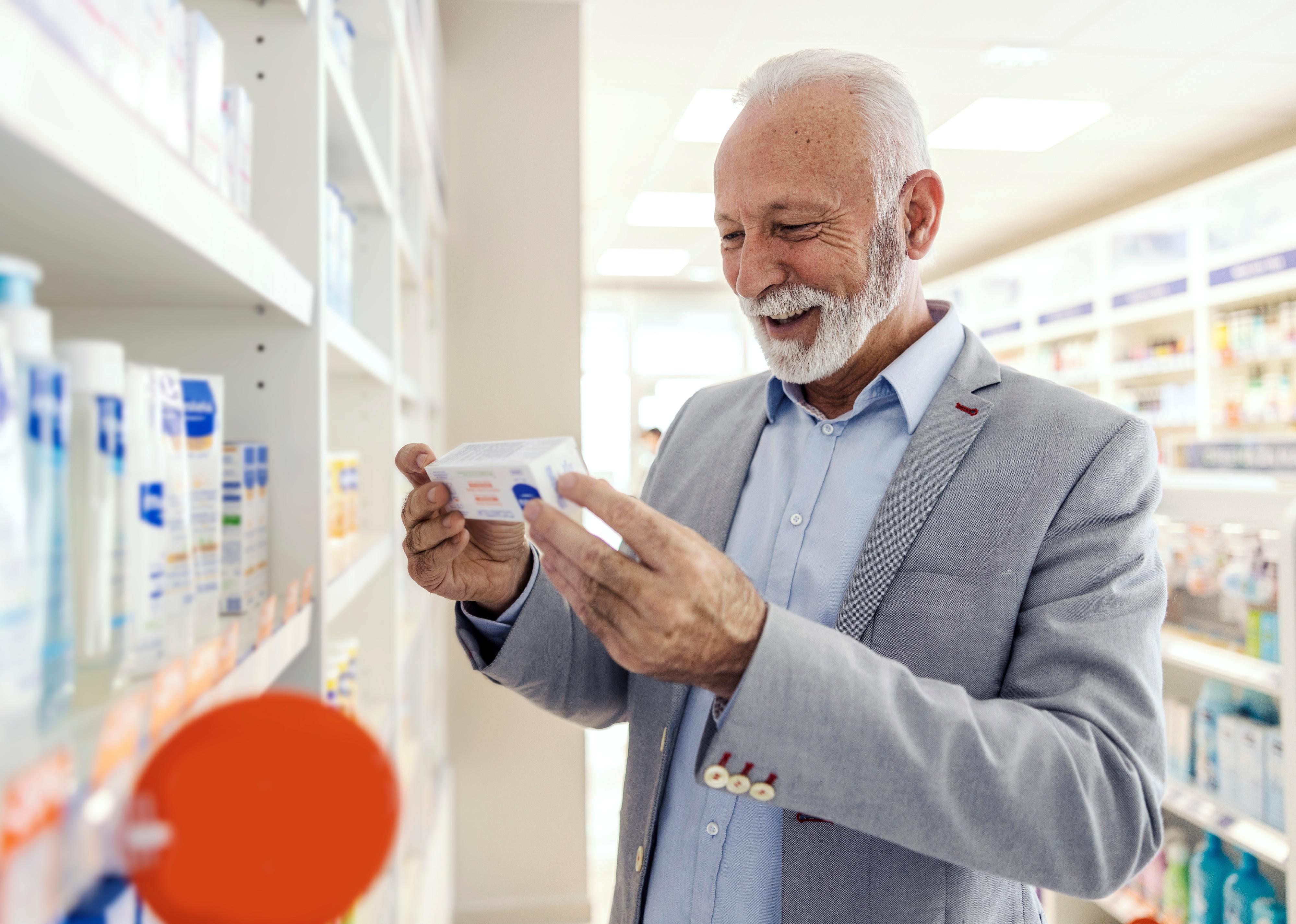 A senior man with a smile holds a package of pills and reads the box.