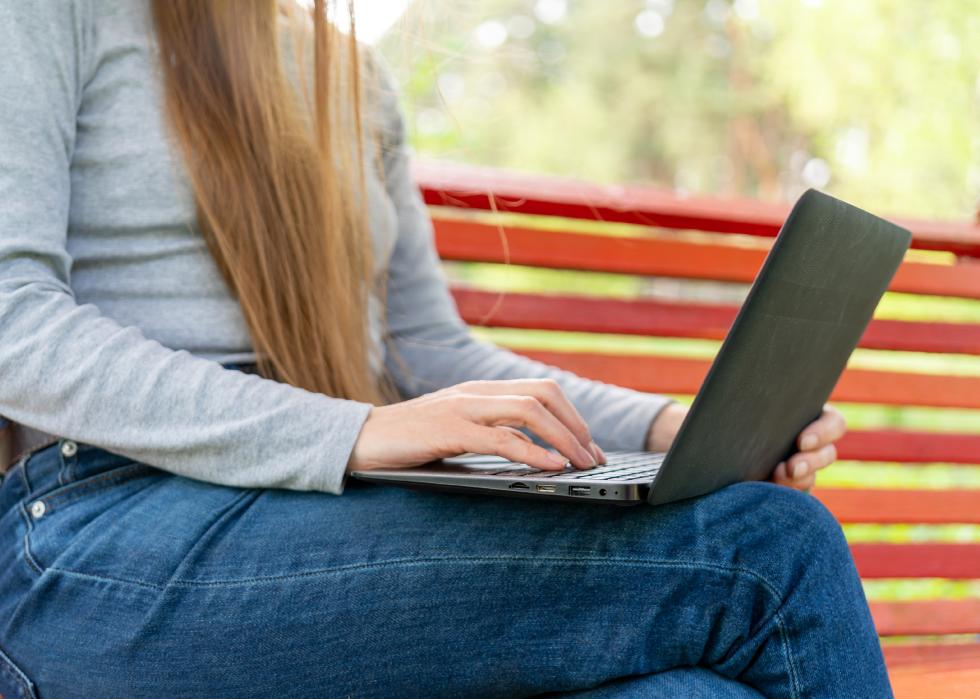A girl holds a laptop on her lap outdoors
