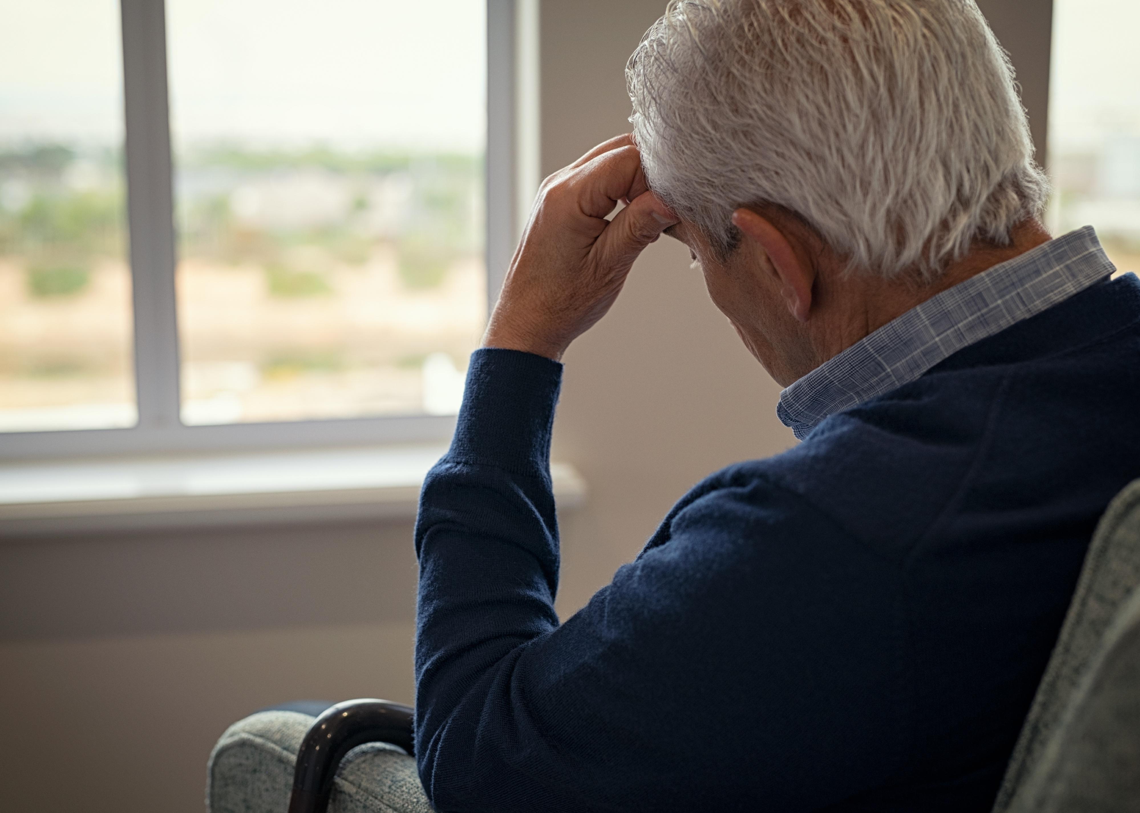 Older man sitting on armchair in living room looking at window.