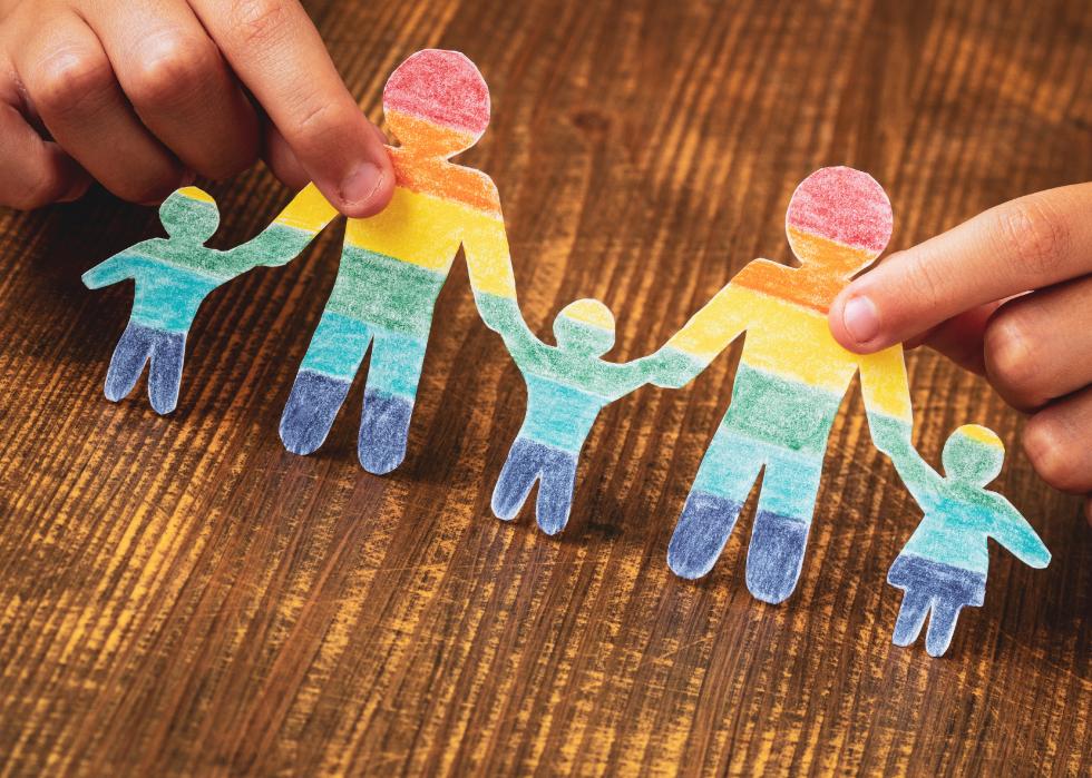 Close up of child's hand holding paper cut out of family in rainbow colors