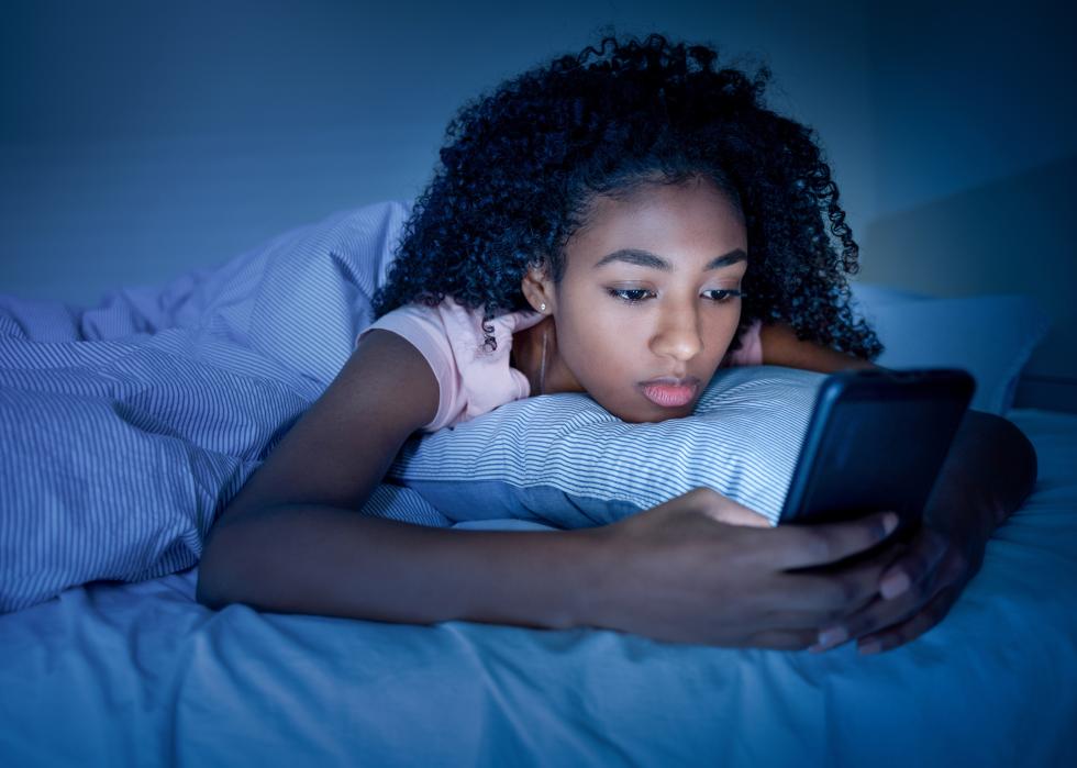 Teen girl using her smartphone in bed in the dark.