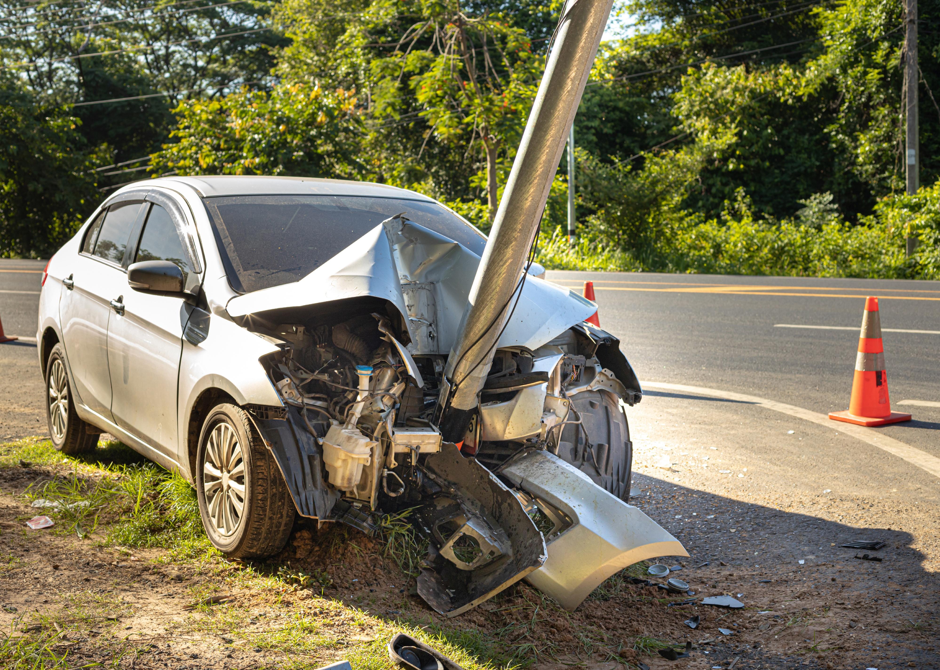 A white sedan after a collision with an electric pole.
