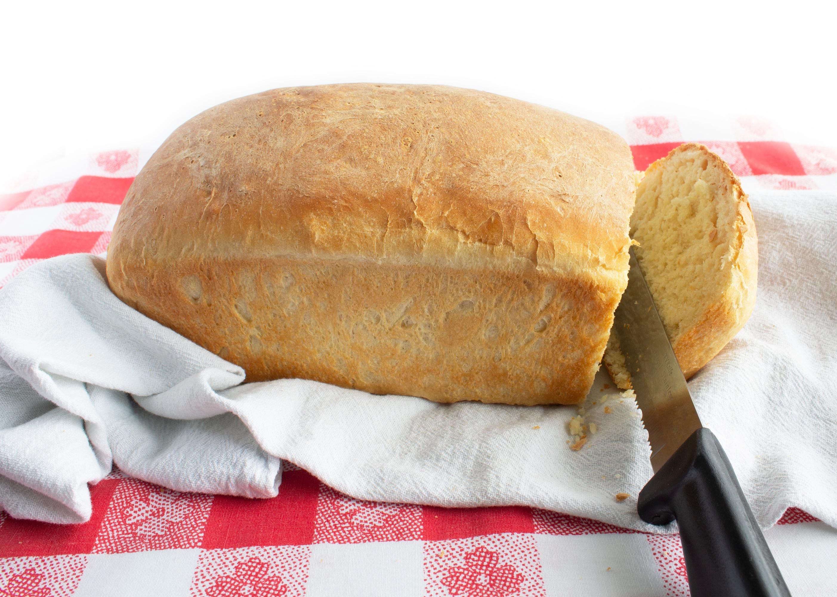 Knife slicing through fresh loaf of bread.