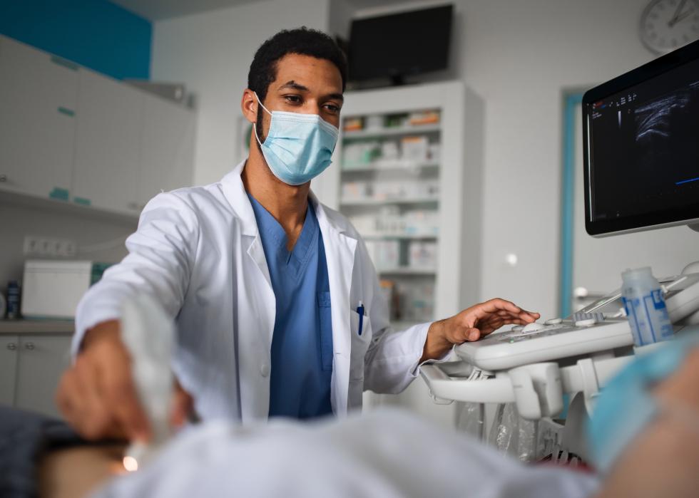 A doctor examining a patient in a bed using ultrasound equipment in a patient's room.