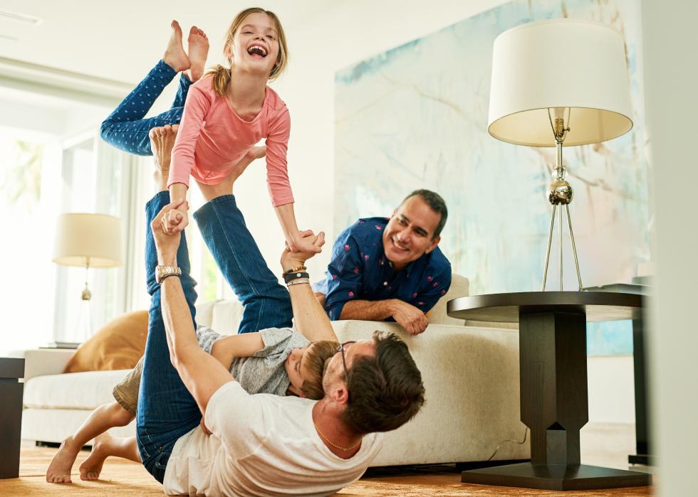 Man laying on couch while other man playing on floor with two kids