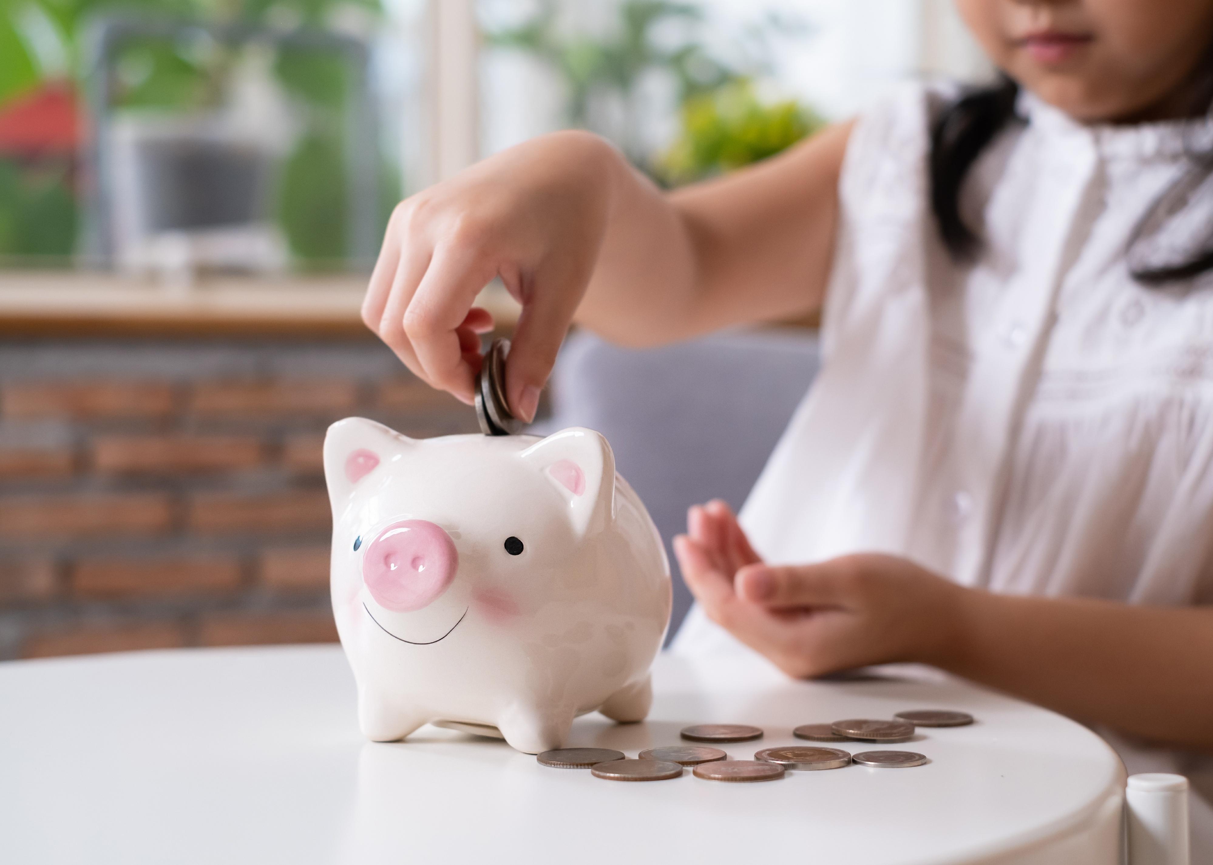 Selective focus of a piggy bank while young girl puts coin in.
