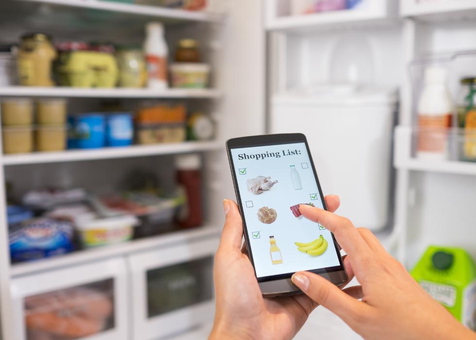 Woman makes a shopping list on phone connected to the refrigerator