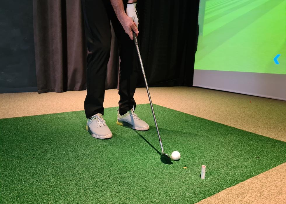 Golf player playing golf indoors on golf simulator closeup.