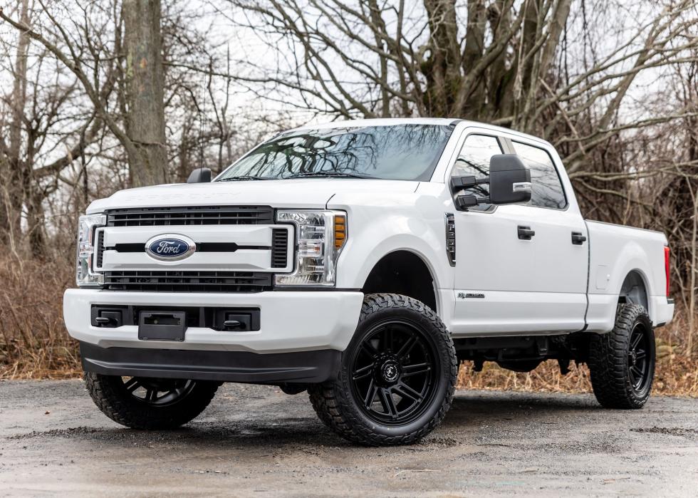 A white 2020 Ford F-250 pickup truck with lifted wheels on a dirt road.