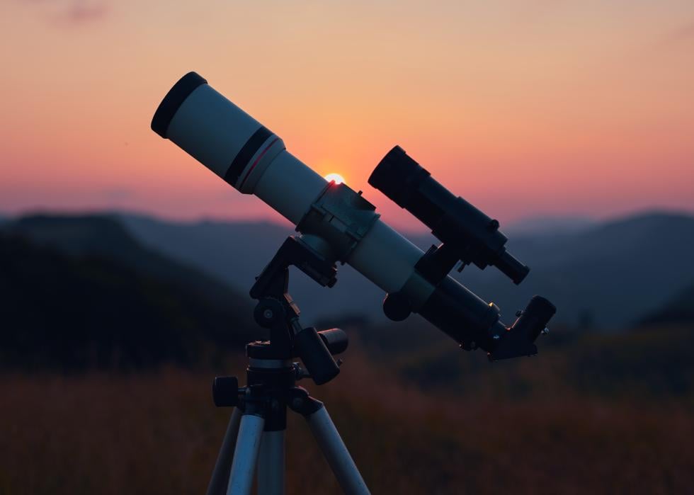 An astronomical telescope set up with a sunset in the background.